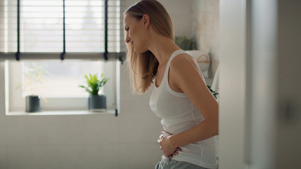 Žena u beloj majici drži stomak zbog menstrualnih bolova