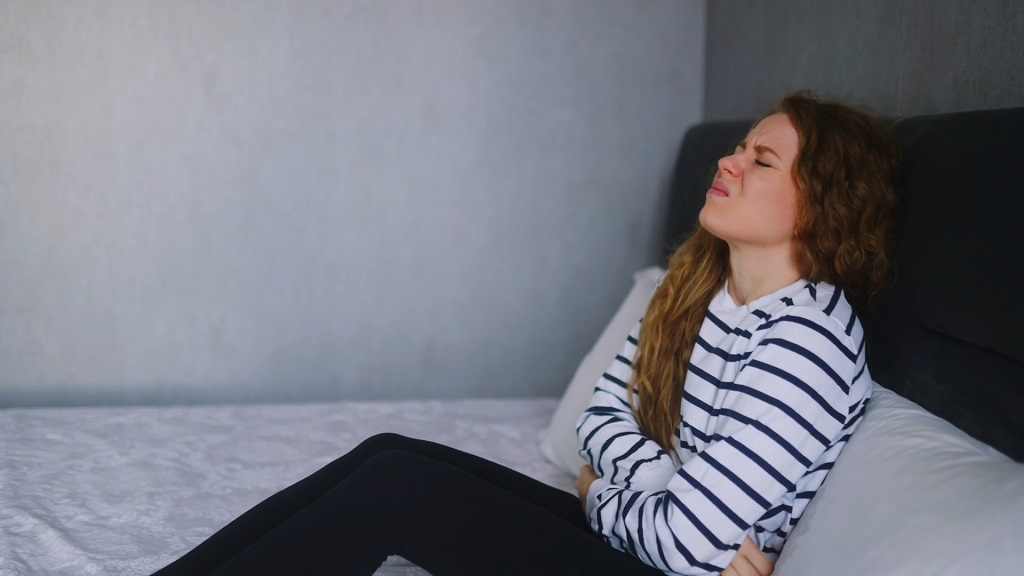 Žena sedi na krevetu i drži stomak zbog jakih menstrualnih bolova
