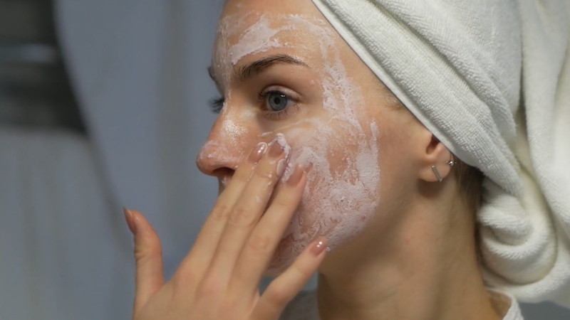 Žena sa peškirom na glavi radi piling na licu